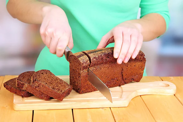 Woman slicing black bread on chopping board on wooden table close up — Stock Photo, Image