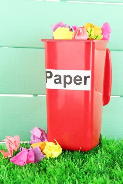 Papelera de reciclaje con papeles sobre hierba sobre fondo azul claro —  Fotos de Stock