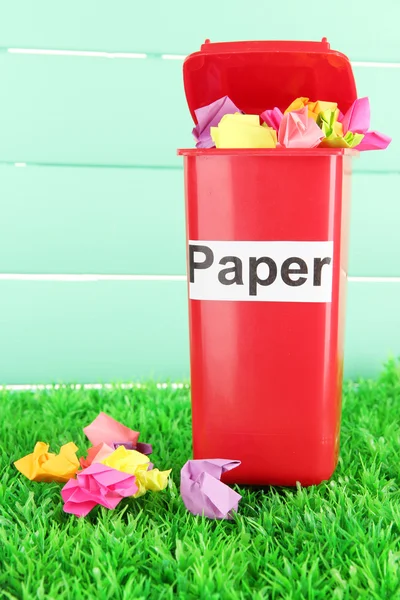 Papperskorgen med papper på gräs på ljusblå bakgrund — Stockfoto