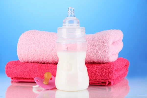 Flasche für Milch mit Handtüchern und Brustwarzen auf blauem Hintergrund — Stockfoto