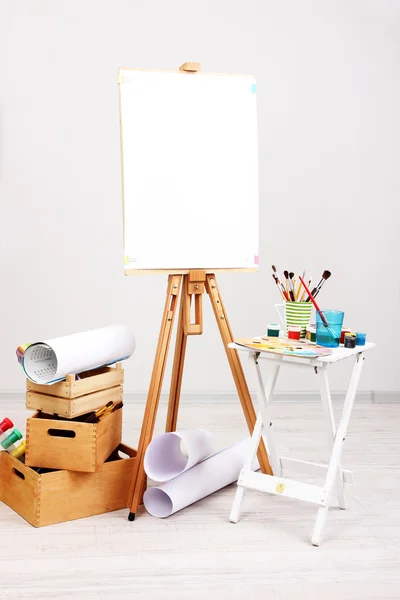 Wooden easel with clean paper and art supplies in room — Stock Photo, Image