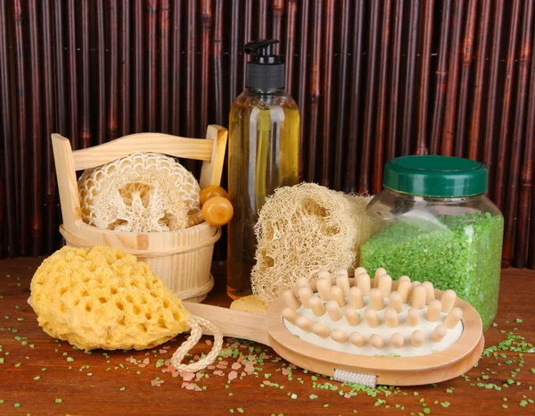 Limpiador, cepillo y cosméticos para ducha sobre mesa de madera sobre fondo de bambú — Foto de Stock