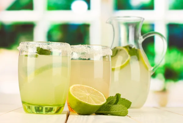 Limonada cítrica en jarra y vasos sobre mesa de madera sobre fondo de ventana — Foto de Stock