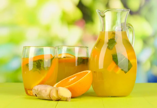 Oransje limonade i krukke og glass på trebord på naturlig bakgrunn – stockfoto