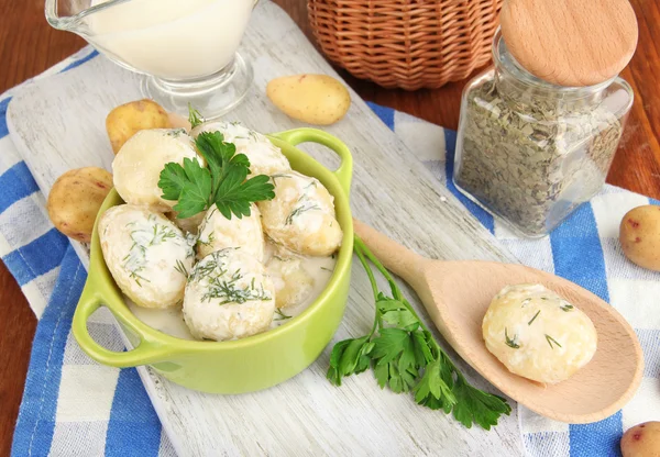 Inschrijving van jonge aardappelen met zure room en kruiden in pan op een houten bord op tabel close-up — Stockfoto