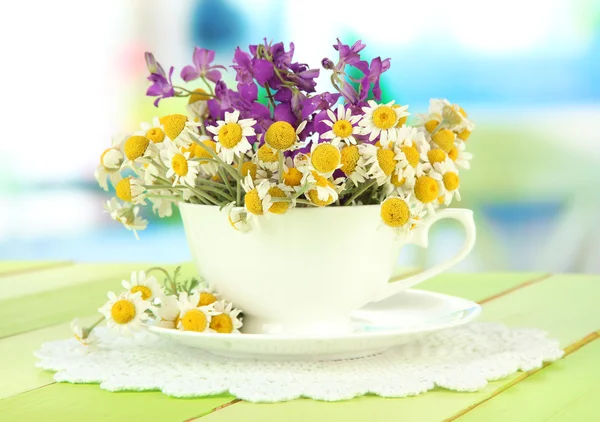 Bouquet of chamomile flowers in cup, on bright background — Stock Photo, Image