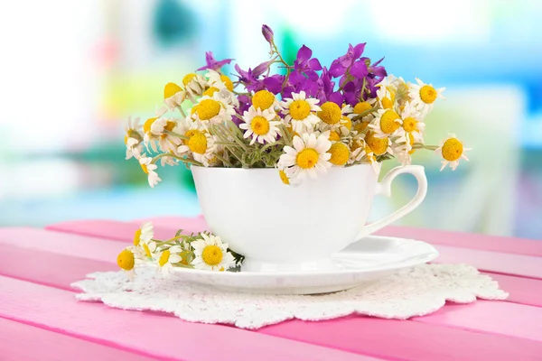 Bouquet of chamomile flowers in cup, on bright background — Stock Photo, Image