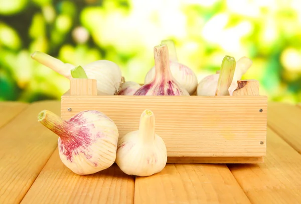 Fresh garlic in box, on wooden table, on bright background — Stock Photo, Image