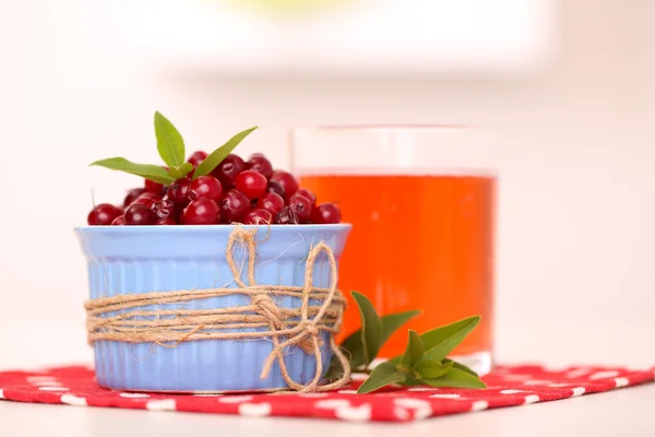 Kieliszek soku żurawinowego i dojrzałe czerwone borówki w misce na stole — Zdjęcie stockowe