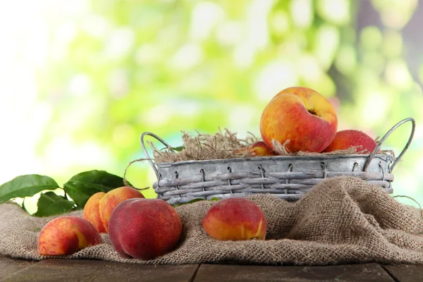 Pêches dans le panier sur sac sur table en bois sur fond nature — Photo