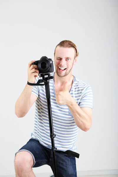 Stilig fotograf med kamera på enbent, på grå bakgrund — Stockfoto