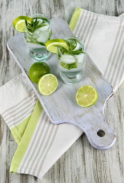 Bicchieri di cocktail con ghiaccio a bordo su tovagliolo su tavolo di legno — Foto Stock