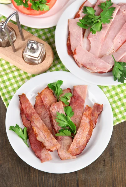 Bacon on plates on napkin on wooden table — Stock Photo, Image