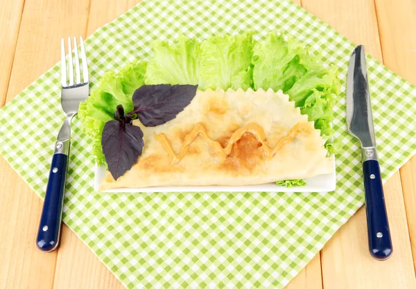 Cheburek savoureux avec des herbes fraîches sur l'assiette, sur fond en bois — Photo