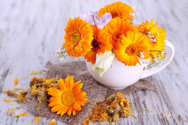 Ringelblumen in Tasse auf Holzgrund — Stockfoto