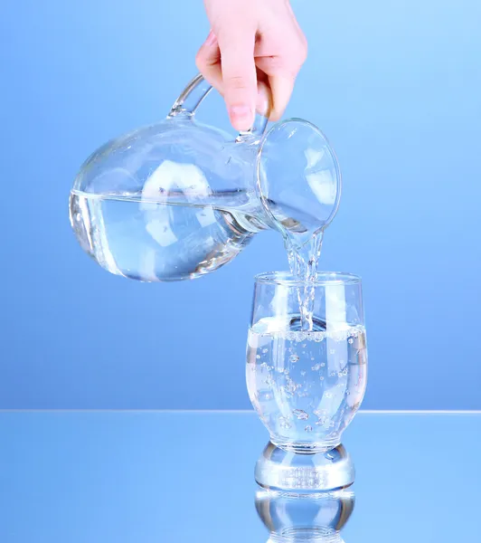 Glass pitcher of water and glass on blue background — Stock Photo, Image