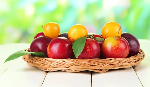 Ripe plums in basket on wooden table on natural background — Stock Photo, Image