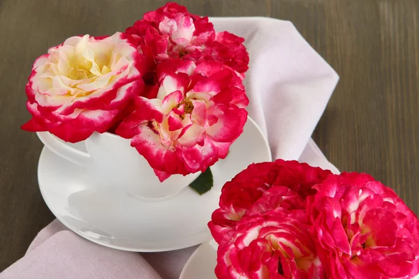 Розы в чашках на салфетке на деревянном фоне — стоковое фото