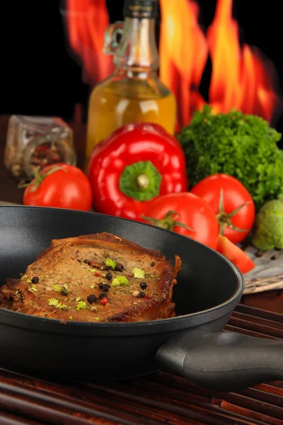 Trozo de carne frita en la sartén en la mesa de madera sobre fondo de fuego —  Fotos de Stock