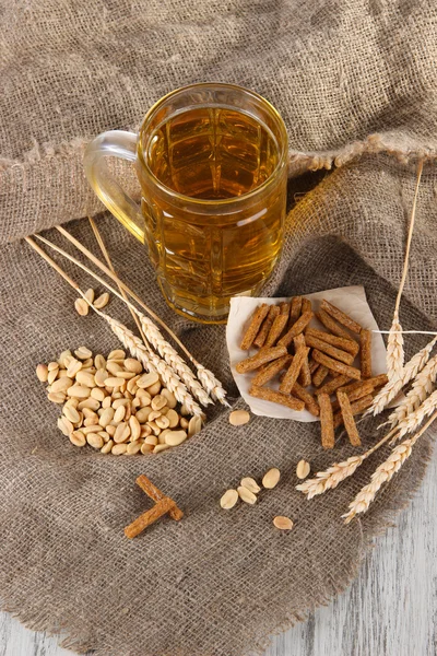 Bier in het glas, crackers en noten op zakken op houten tafel — Stockfoto