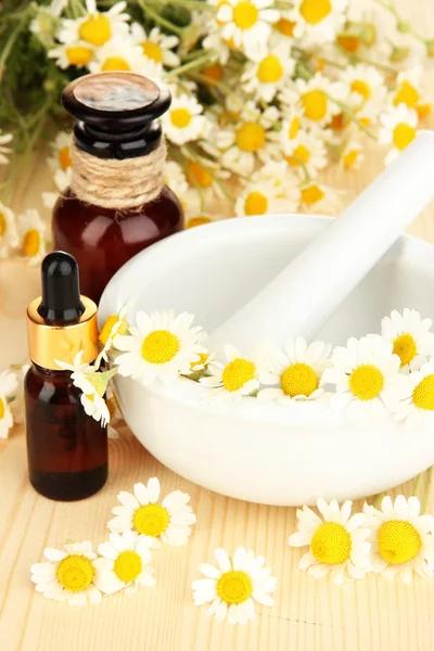 Aceite esencial y flores de manzanilla en mortero sobre mesa de madera —  Fotos de Stock