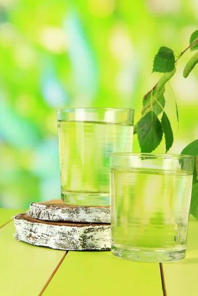 Glazen birch sap op houten tafel, op groene achtergrond — Stockfoto