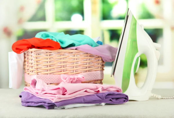Steam iron and wicker basket with clothes, on bright background — Stock Photo, Image
