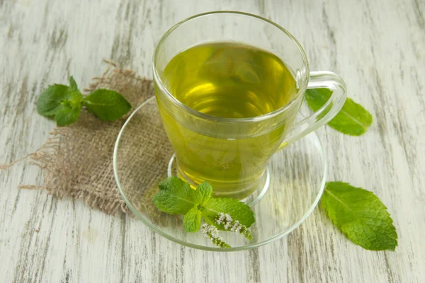 Tetera y taza de té de hierbas con flores de menta fresca en la mesa de madera —  Fotos de Stock