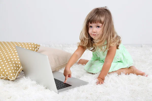 Pequena menina bonito sentado no tapete com laptop, no fundo cinza — Fotografia de Stock