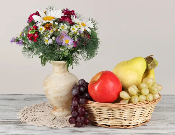 Beautiful bright flowers in vase with fruits on table on gray background — Stock Photo, Image