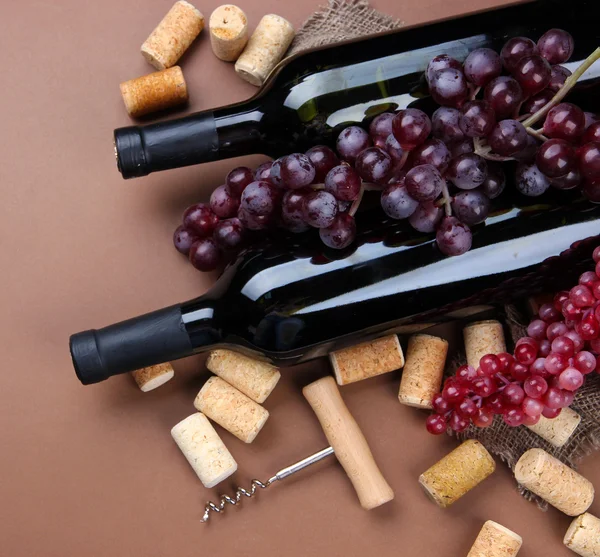 Botellas de vino, uvas y corchos sobre fondo marrón —  Fotos de Stock