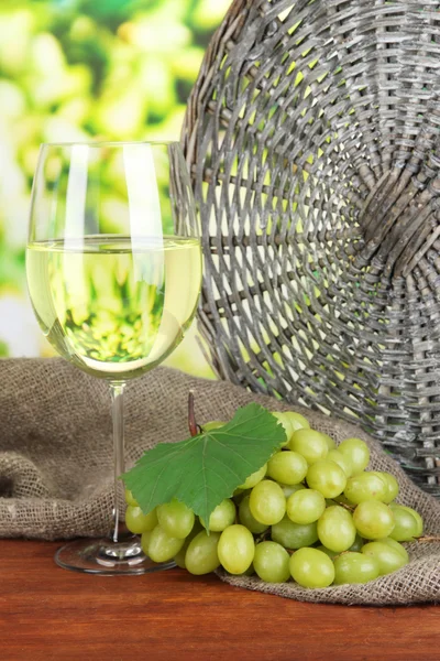 Maturare deliziose uve con un bicchiere di vino sul tavolo su sfondo brillante — Foto Stock