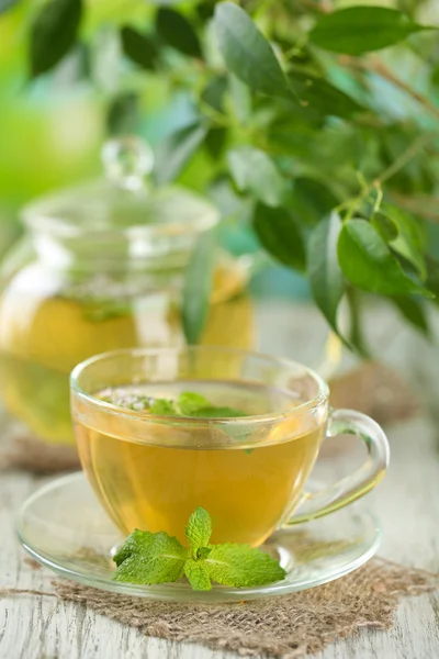 Tetera y taza de té de hierbas con flores de menta fresca en la mesa de madera — Foto de Stock