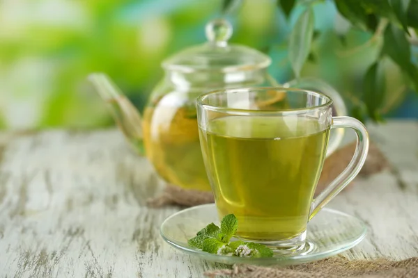 Teiera e tazza di tisana con fiori di menta freschi sul tavolo di legno — Foto Stock