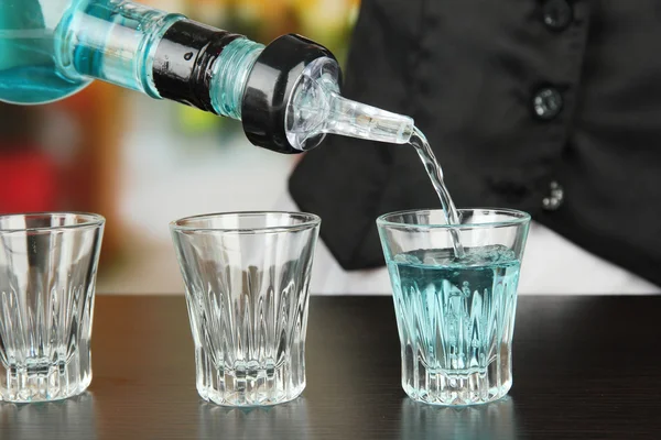 Barmen hand with bottle pouring beverage into glasses, on bright background — Stock Photo, Image