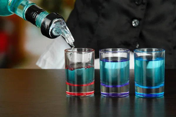 Barman mano con bottiglia versando bevanda in bicchieri, su sfondo luminoso — Foto Stock