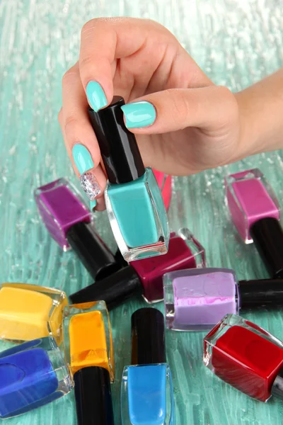Belas mãos de mulher com manicure azul e várias garrafas com esmalte, em fundo de cor — Fotografia de Stock
