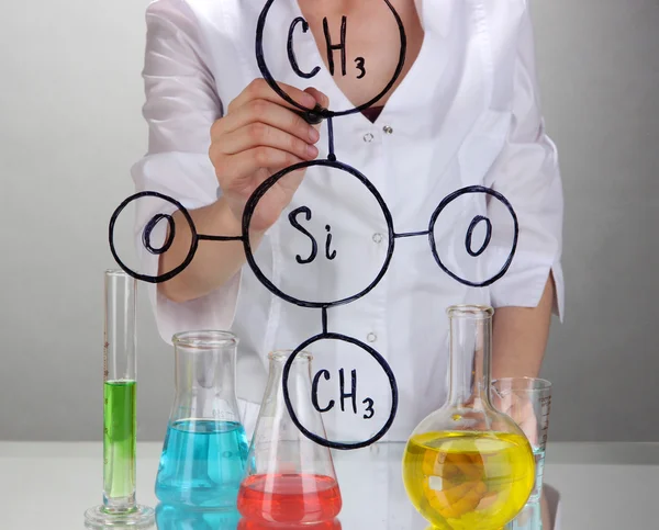 Kemist kvinna skriva formler på glas på grå bakgrund — Stockfoto