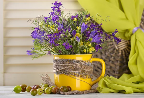 Beautiful bouquet of wildflowers in cup and berries on wooden table — Stock Photo, Image