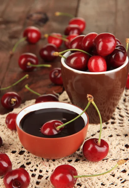 Спелые красные ягоды вишни в чашке и шоколадный соус на деревянном столе крупным планом — стоковое фото