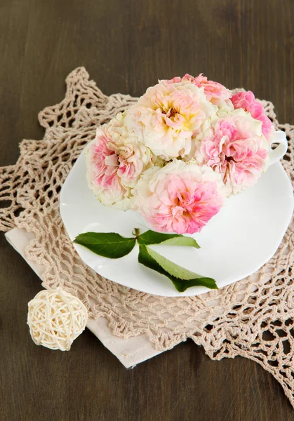 Roses in cup on napkins on wooden background — Stock Photo, Image