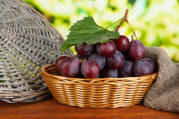 Ripe delicious grapes in wicker basket on table on bright background — Stock Photo, Image