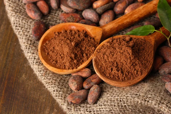 Poudre de cacao dans des cuillères et fèves de cacao sur fond en bois — Photo