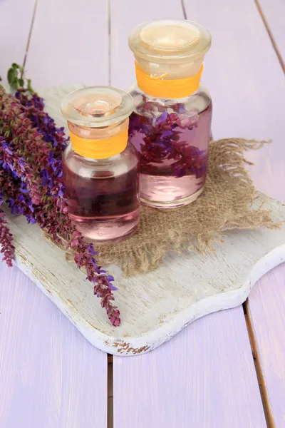 Geneeskundeflessen met salvia bloemen op paarse houten achtergrond — Stockfoto