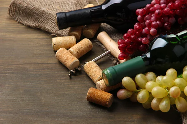 Botellas de vino, uvas y corchos sobre fondo de madera — Foto de Stock