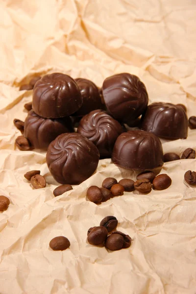 Шоколадные конфеты и кофейные зёрна, на бежевом бумажном фоне — стоковое фото