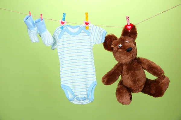 Baby clothes hanging on clothesline, on green background