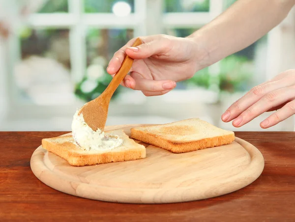 Процес приготування ролів салямі на смаженому хлібі, на яскравому фоні: жіноча рука мазає сирним кремом на смаженому хлібі — стокове фото