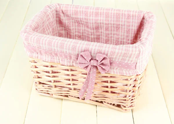 Wicket basket with pink fabric and bow, on color wooden background — Stock Photo, Image