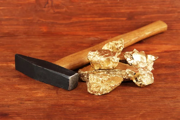 Golden nuggets with hummer on wooden background — Stock Photo, Image